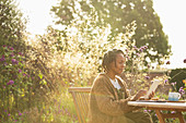 Woman using digital tablet at sunny garden patio table