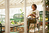 Woman with smartphone drinking tea in greenhouse