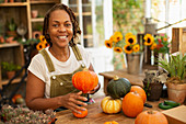 Happy female florist arranging autumn pumpkins in shop