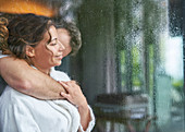 Affectionate romantic couple hugging at rainy window