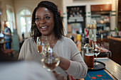 Smiling woman drinking white wine with friend at bar