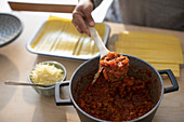 Woman with tomato sauce making fresh lasagne at home