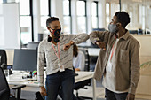 Business people in face masks elbow bumping in office