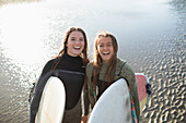Happy young female surfers with surfboards on wet beach