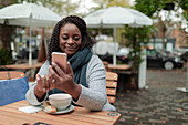 Woman with coffee using smartphone at table on cafe patio