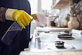 Woman in gloves cleaning kitchen stove with spray cleaner