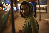 Confident young woman in hoodie on city sidewalk at night
