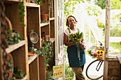 Happy female florist with flower bouquet in shop doorway