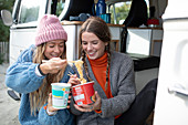Young friends sharing instant noodles at camper van doorway