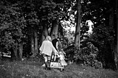 Parents holding hands with daughters walking near trees