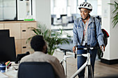 Woman in helmet with bicycle talking to coworker in office