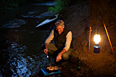 Fisherman cooking fish on camping stove at night