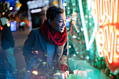 Woman with Christmas bags looking at neon storefront