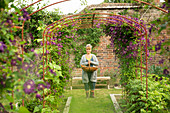 Woman with basket under garden trellis with purple flowers