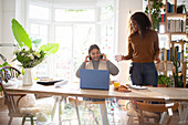 Daughter serving coffee to mother working at laptop on table