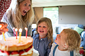 Happy mother and daughters celebrating birthday with cake