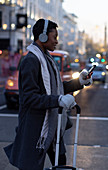 Woman with suitcase and smartphone crossing city street