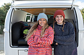 Happy young women friends in knit hats at back of camper van
