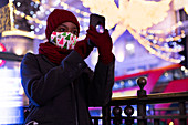 Woman in Christmas mask taking selfie among city lights