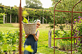 Woman carrying basket of harvested vegetables in garden