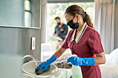 Hotel maid in facemask and gloves cleaning hotel bathroom