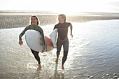 Happy young female surfers running with surfboards on beach