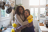 Mother and daughter in rubber gloves hugging in kitchen