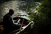 Man with tablet fly fishing and video chatting in boat