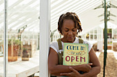 Female garden center owner with open sign in greenhouse