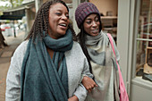 Happy mother and daughter walking arm in arm outside store