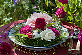 Arrangement of rose petals and love-in-a-mist in a wreath of grass on a flat dish