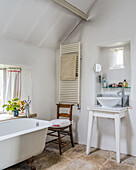Wachschüssel auf weißem Tisch, Handtuchtrockner, alter Stuhl und freistehende Badewanne im Badezimmer