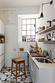 Narrow kitchen with white subway tiles, wooden shelves, lattice windows and wooden stool