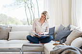 Blonde Frau liest ein Buch auf gemütlichem Sofa sitzend
