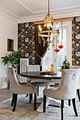 Elegant dining room with round table and upholstered chairs, in the background a statement wall with floral wallpaper