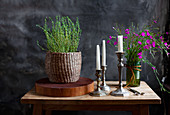 Bouquet of wild Carthusian pinks and grass, basket of thyme on a wooden disc and silver candle holder