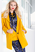 A blonde woman wearing a yellow coat, a blue patterned scarf and matching trousers