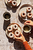 Hände halten einen Donut und eine Tasse Kaffee