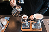 Midsection of barista pouring water in coffee filter at cafe