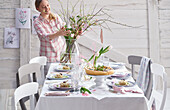 A young woman arranging a bouquet of flowers at a spring table laid with hors d'oeuvres
