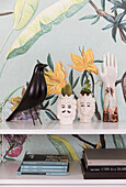 Shelf with decorative objects and books in front of botanical wallpaper
