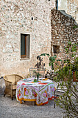 Set table with colorful tablecloth on graveled area in front of natural stone house