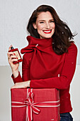 Brunette woman in red jumper with a perfume bottle and a Christmas present