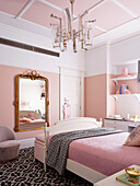 Girls room in white and pink tones with bed, gold-framed mirror and desk