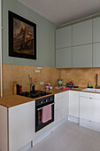 L-shaped kitchen counter below wooden splashback and vintage painting