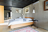 King size bed in the bedroom with concrete walls, ensuite bathroom in the background
