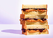 Stack of peanutbutter and jelly sandwiches with raspberry jam on a light purple background