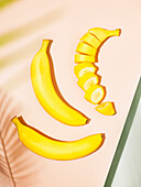 Two whole and one sliced banana on geometric, pastel surfaces with palm leaf shadows.