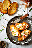 A plate of crostini topped with prosciutto ham, taleggio cheese and fresh herbs