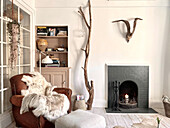 Living room with comfortable armchairs, shelves, decorative branches and antlers over a fireplace